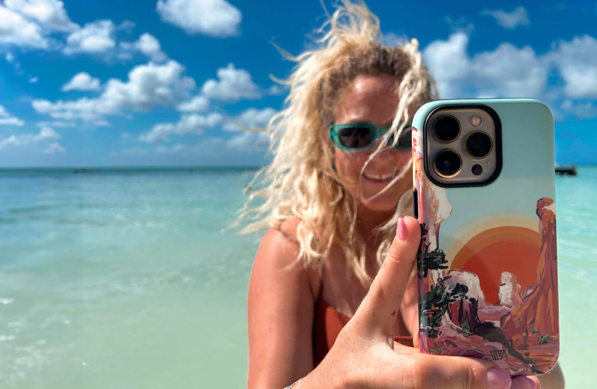Woman at the beach holding up her phone in a Trovvve case with a desert sunset art print